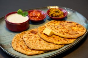 Appetizing Indian paratha served with yogurt and pickles on a blue plate.