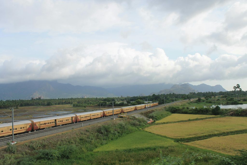 A passenger train traverses a lush rural landscape under a cloudy sky.
